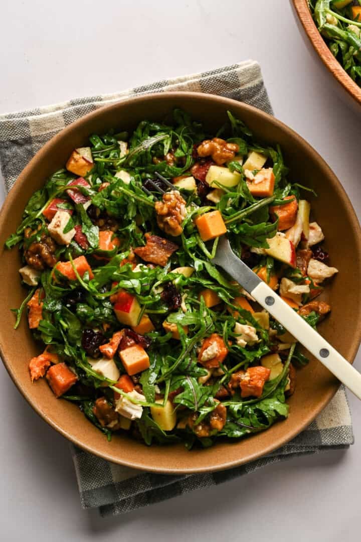 Ovanifrån av bacon äpple cheddar ruccolasallad i en brun skål med en gaffel i.
