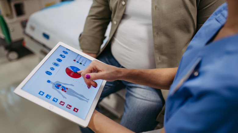 En person i scrubs pekar på ett sjökort på en iPad-skärm till en man på en bår.