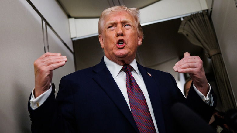 President Donald Trump underifrån, han gestikulerar med båda händerna, munnen inklämd i ett o medan han pratar på Air Force One.