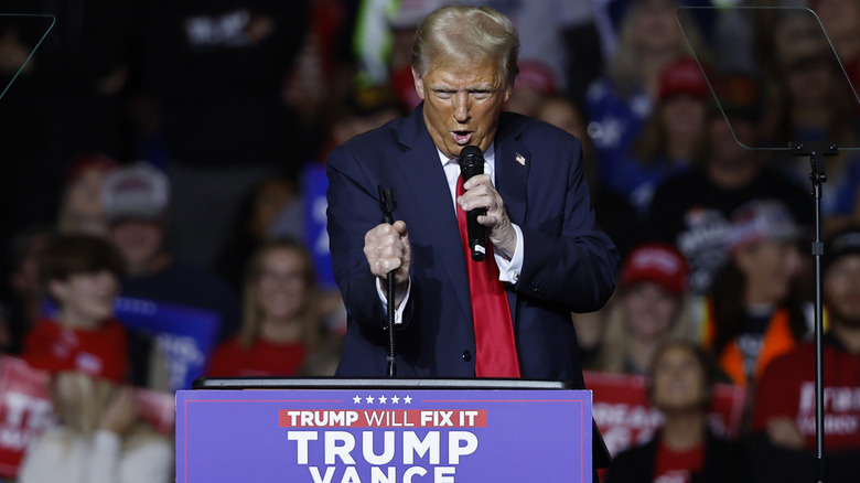 Donald Trump pratar i en mikrofon i ett rum fullt av människor och står bakom ett podium.