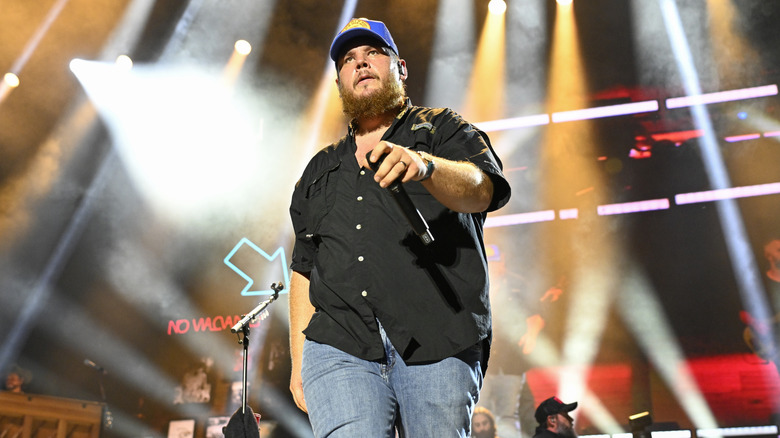 Luke Combs håller en mikrofon som går på scenen