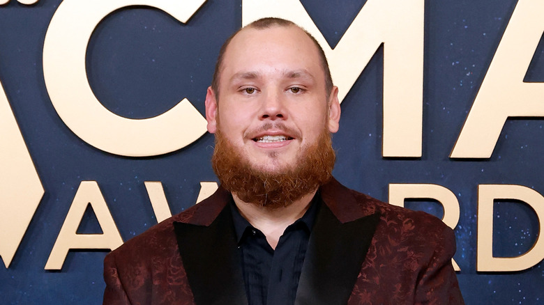 Luke Combs i en röd kostymrock framför ACMA Awards logotyp