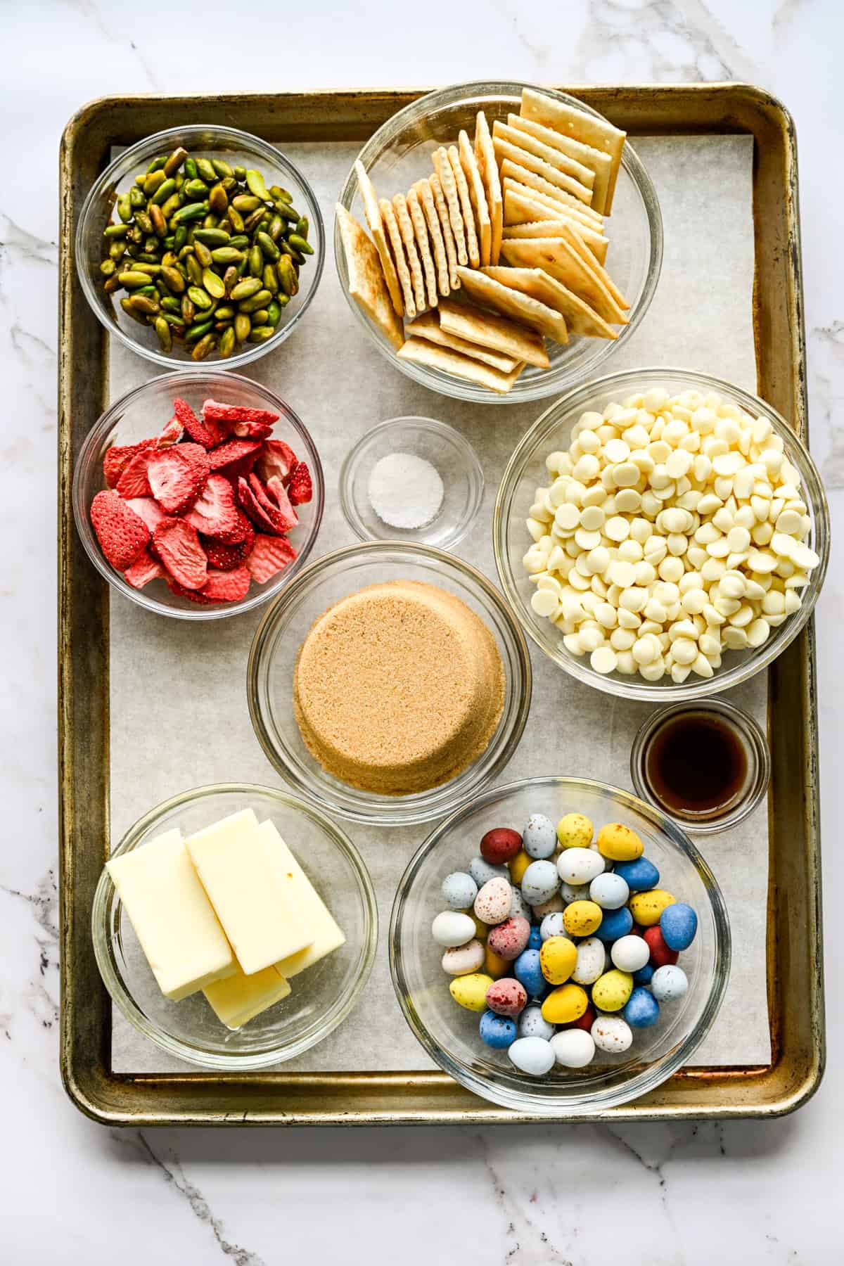 Vy ovanifrån av ingredienser för påskcrack, inklusive vita chokladchips, smör och socker.