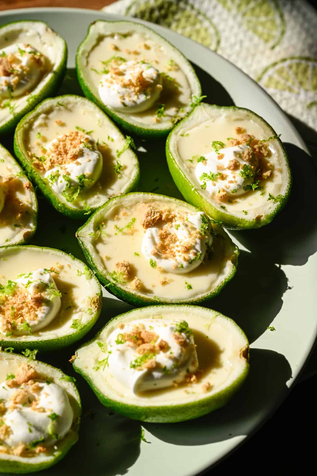 Närbild av limepossets toppade med vispad grädde och graham cracker smulor på ljusgrön tallrik. 