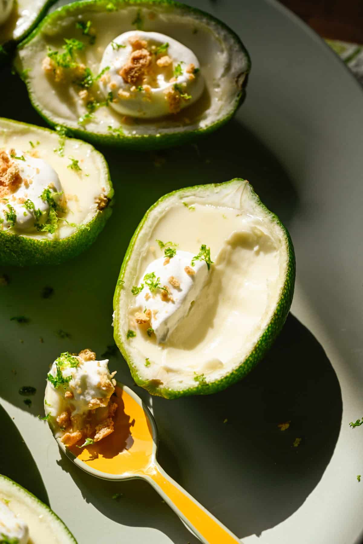 Närbild av limeposset toppad med vispad grädde och graham cracker smulor på ljusgrön tallrik med en sked uttagen.