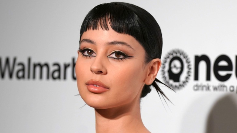 Närbild av Alexa Demie vid ett evenemang 2020. Hon har en dramatisk ögonlook med tjock svart eyeliner och hennes hår är slickat tillbaka till en bulle - hennes microbangs är utelämnade.