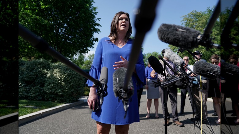 Sarah Huckabee Sanders talar till reportrar i en blå skiftklänning med klockärmar