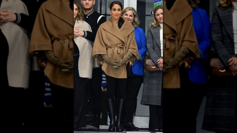Meghan Markle klädd i ljusbrun mantel med svarta skräddarsydda byxor och höga ridstövlar i läder på Invictus One Year to Go-evenemanget.