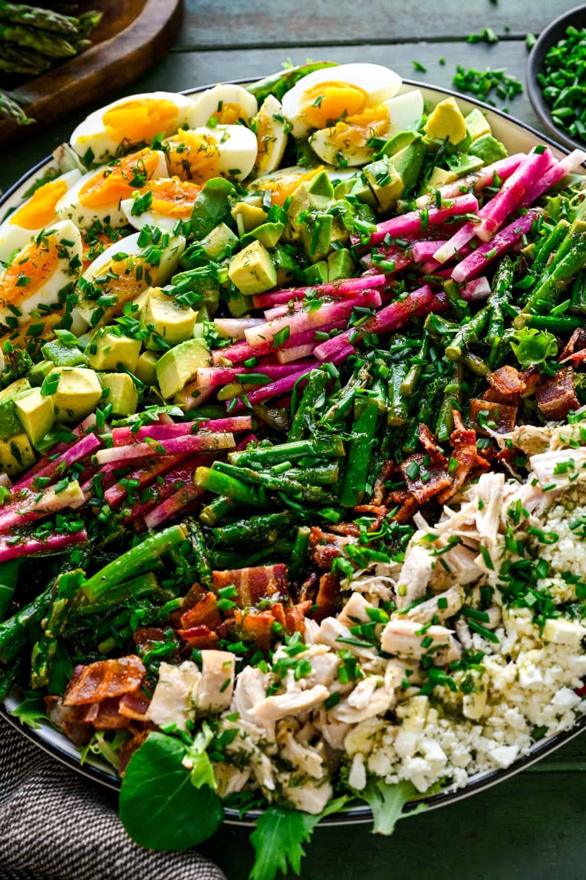 Närbild av våren cobb sallad med hårt kokt ägg, avokado, rädisa, sparris, bacon, kyckling och fetaost i rader.