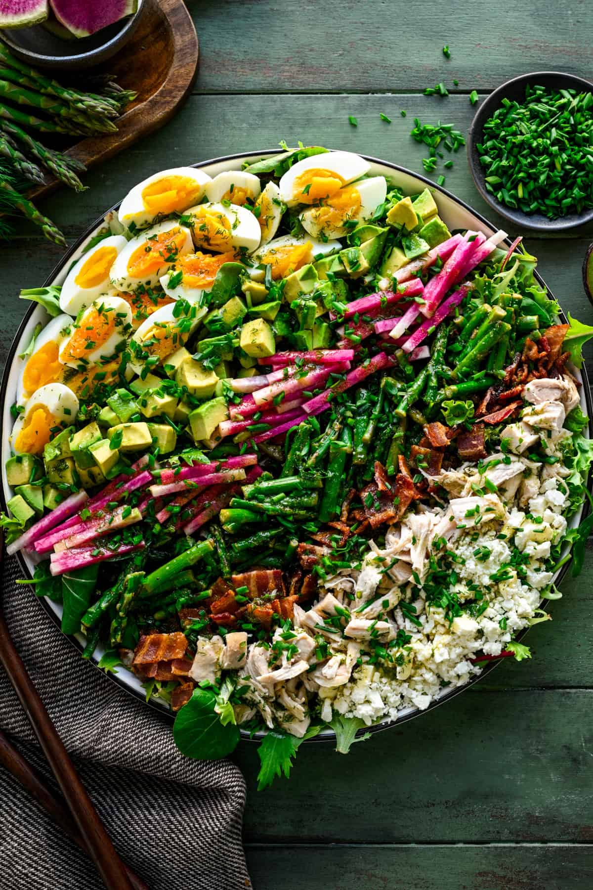 Ovanifrån av våren cobb sallad med hårdkokt ägg, avokado, rädisa, sparris, bacon, kyckling och fetaost i rader.