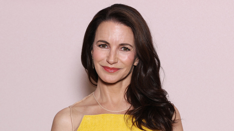 Kristin Davis bär en knallgul klänning och en djärv röd läpp medan hon poserar framför en ljusrosa bakgrund