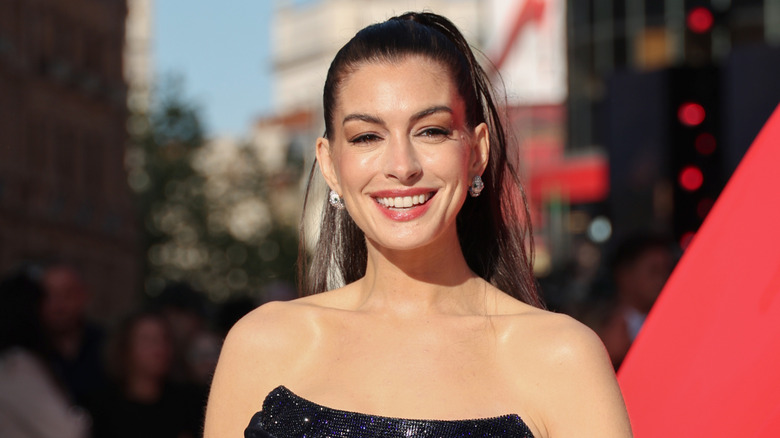 Anne Hathaway ler på ett soligt foto taget på ett utomhusevenemang på röda mattan