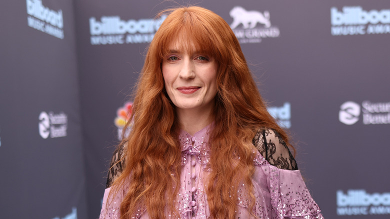 Florence Welch ler vid ett evenemang på röda mattan medan hon bär en ljusrosa klänning med spetsärmar