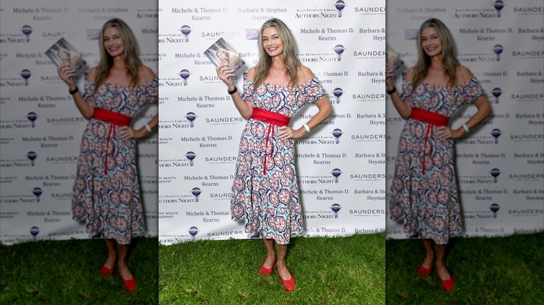 Paulina Porizkova står på gräset och håller en bok och bär röda skor och en klänning på ett evenemang.