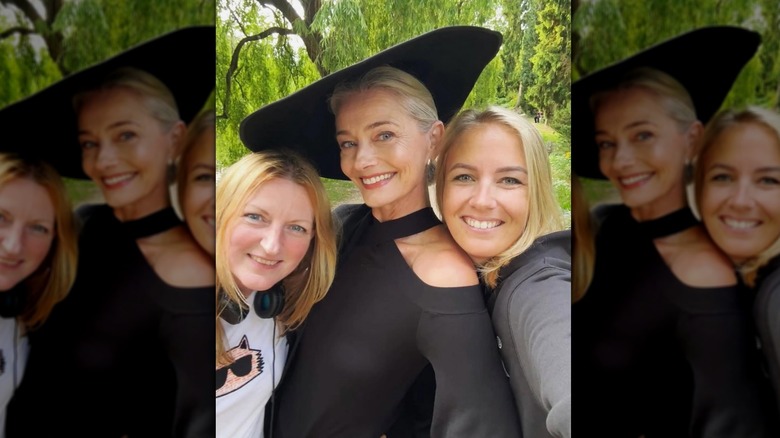Paulina Porizkova poserar utanför bredvid två blonda kvinnor för en selfie i svart klänning och platt hatt.
