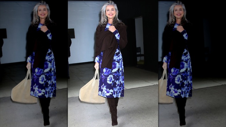 Paulina Porizkova går i en blå blommig klänning och svart tröja och stövlar.
