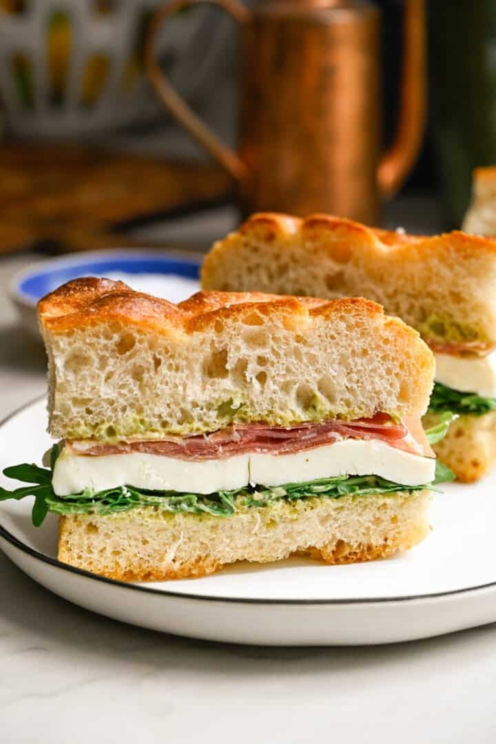 Närbild från sidan av en focaccia smörgås med pesto aioli, ruccola, färsk mozzarella och prosciutto. 