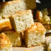 Närbild av 3 stycken hemmagjord focaccia staplade på bakplåtspapper.