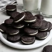 Närbild från sidan av hemgjorda oreos staplade på en vit platta med ett glas mjölk bakom.