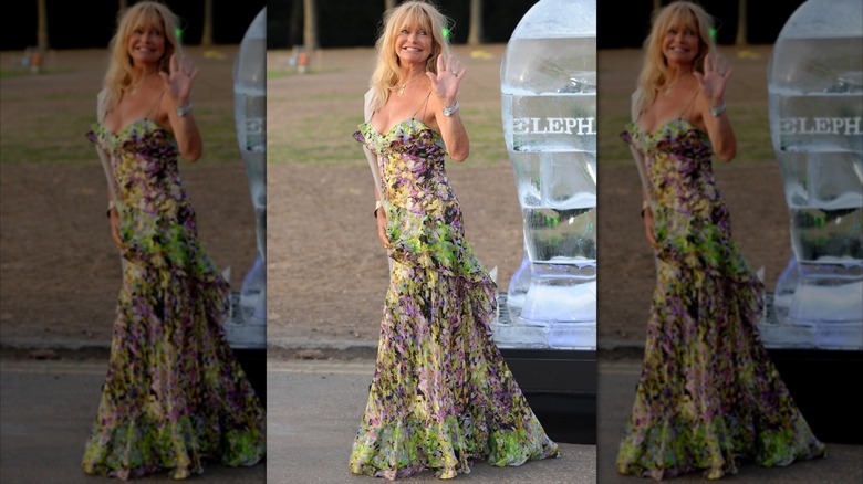 Goldie Hawn vinkar utanför i en färgglad flödande klänning.