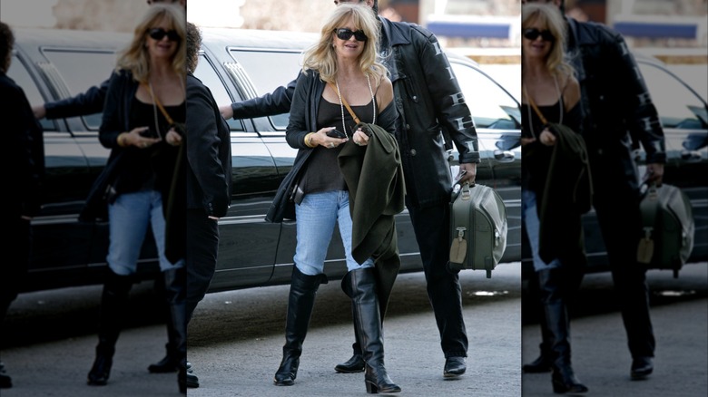 Goldie Hawn fotograferade nära en bil på en gata klädd i jeans, svarta stövlar, en svart topp och solglasögon.