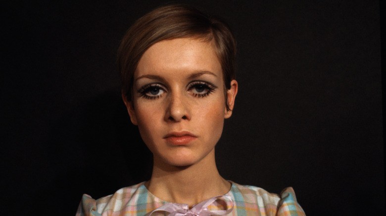 Twiggy poserar för en fotografering med djärv ögonmakeup och en ginghamskjorta