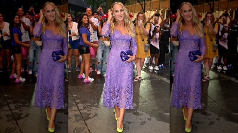 Sarah Jessica Parker poserar på ett event 2023 med handen vid huvudet iförd en lila spetsklänning.