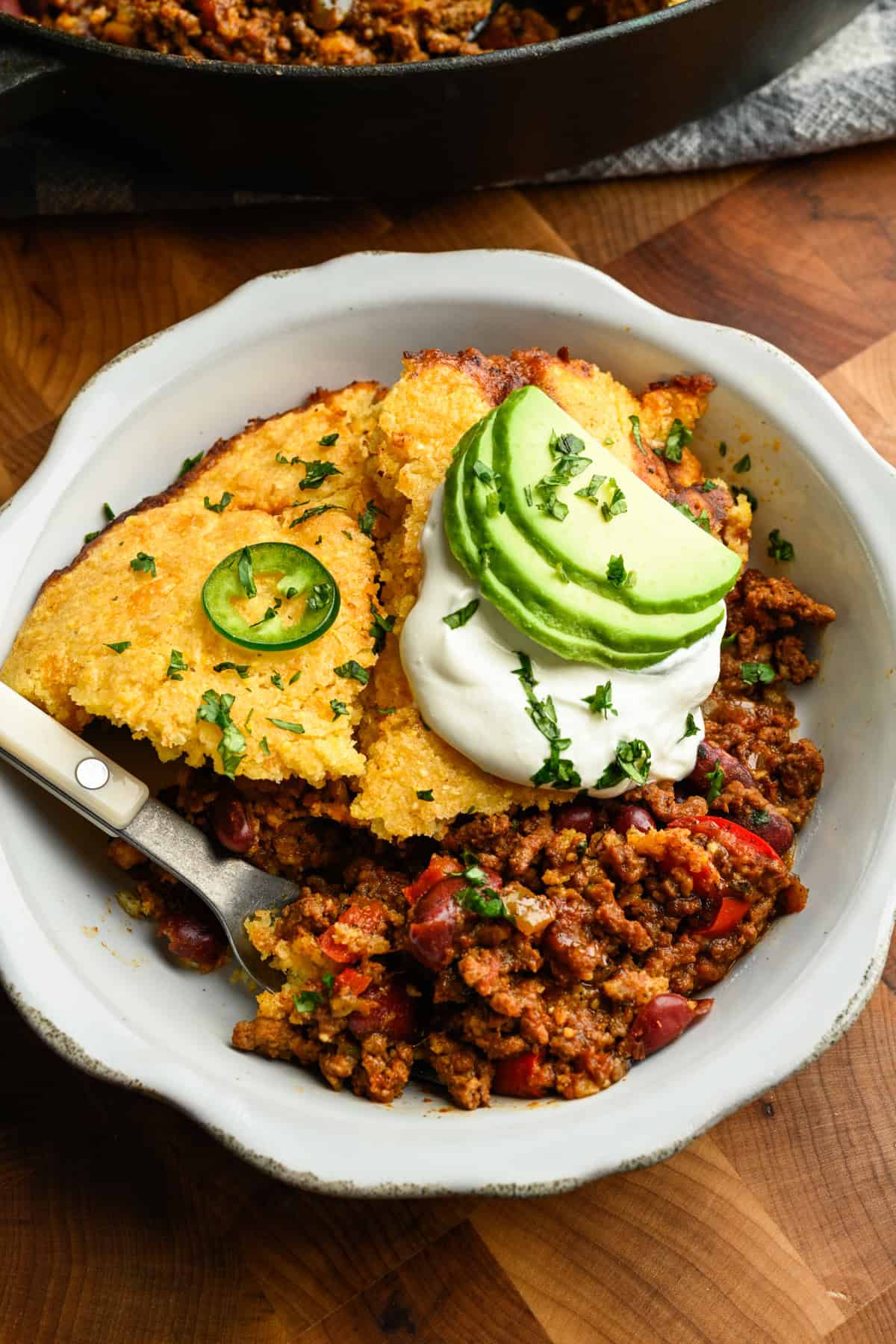 Chilipaj toppad med majsbröd i en vit skål med avokadoskivor.