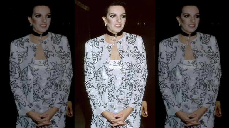 Liza Minnelli poserar med händerna knäppta iklädd en vit och svart outfit och ett svart chokerhalsband.