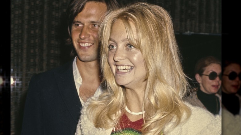 Goldie Hawn ler utan smink iklädd en vit tröja och ett vitt halsband.