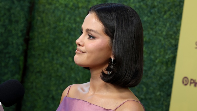 Selena Gomez poserar framför en grön bakgrund på ett event, med en snygg bob-frisyr.