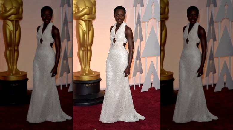 Lupita Nyong'o ler iklädd en vit pärlklänning