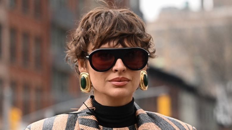 En kvinna som bär solglasögon, stora örhängen och håret i en vågig pixie cut