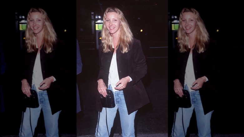 Lisa Kudrow klädd i jeans, en vit skjorta och en svart jacka, med långt vågigt hår.