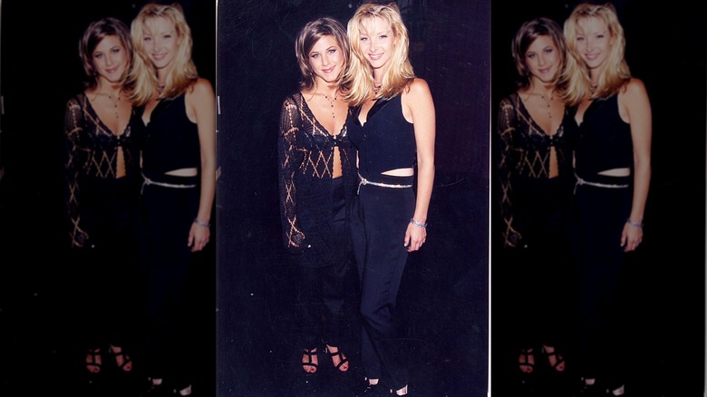 Lisa Kudrow i svarta byxor och en svart miniväst poserar bredvid Jennifer Aniston.