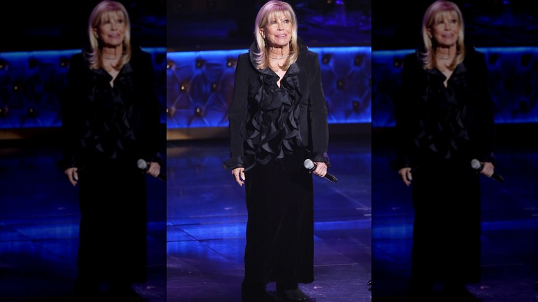 Nancy Sinatra håller i en mikrofon på scenen iförd en svart volang topp och en svart kjol.
