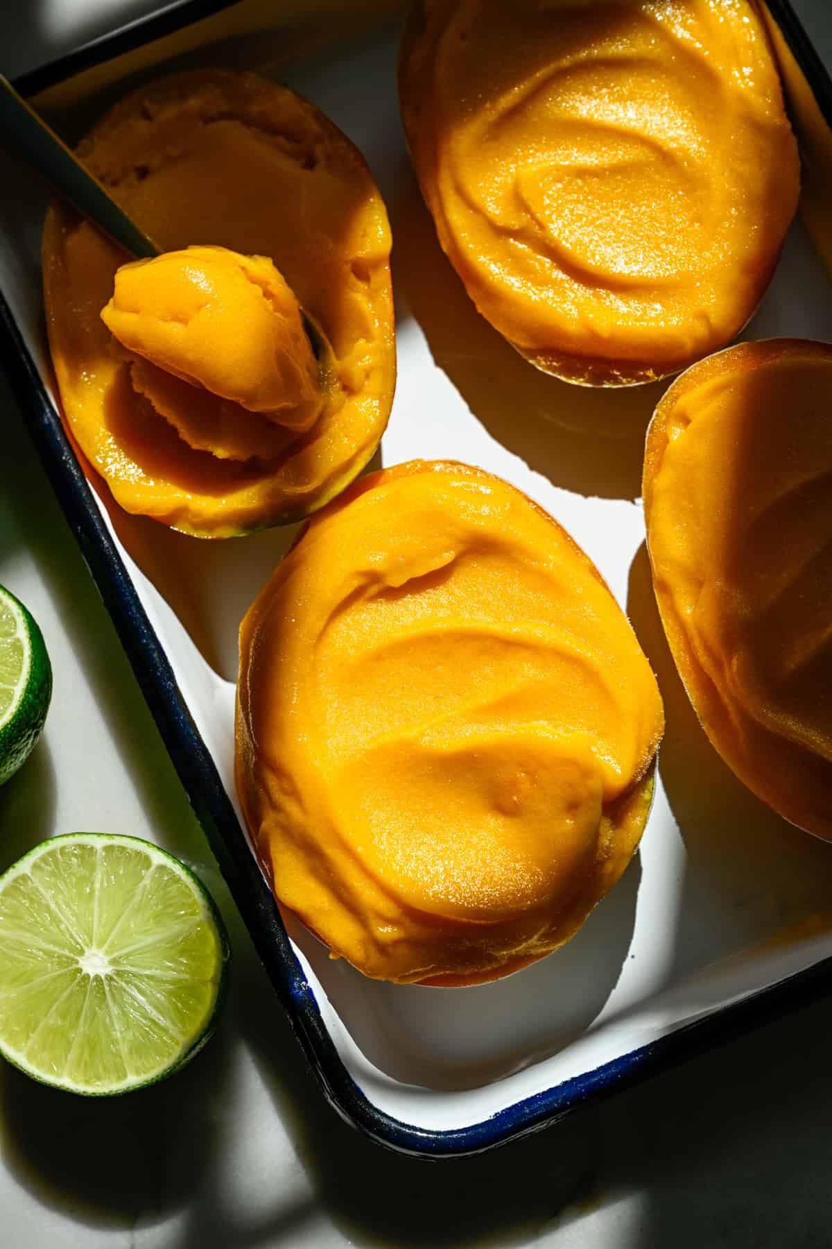 Vy ovanifrån av mangosorbet i en mangohalva på en plåt med några andra.