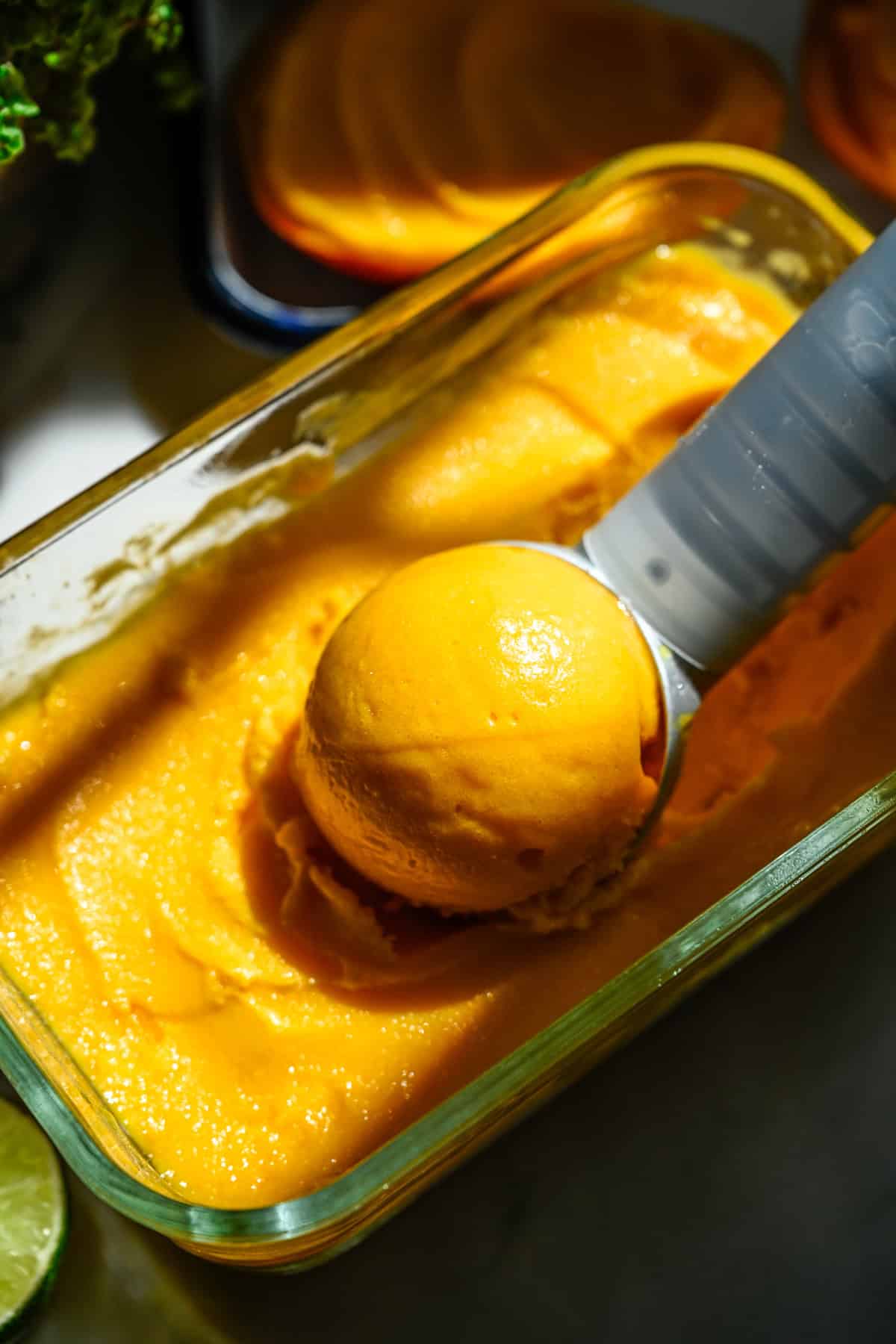 Närbild av en skopa mangosorbet som sitter i en behållare med sorbet.