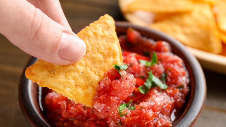 Person som doppar nachochips i kryddig salsasås vid bordet