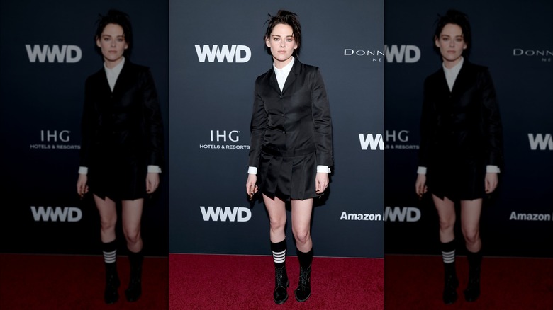 Kristen Stewart klädd i en svart kavajklänning med svarta skor vid ett evenemang på röda mattan.