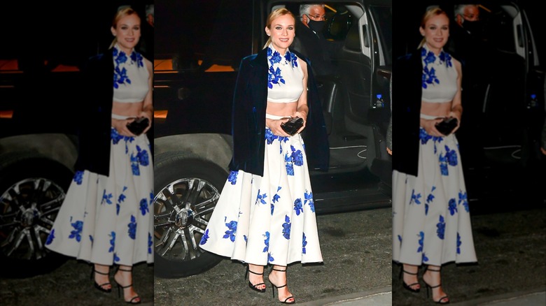 Diane Kruger vid ett event klädd i en vit-blå blommig crop-top och en kjol med en mörkblå sammetsjacka.