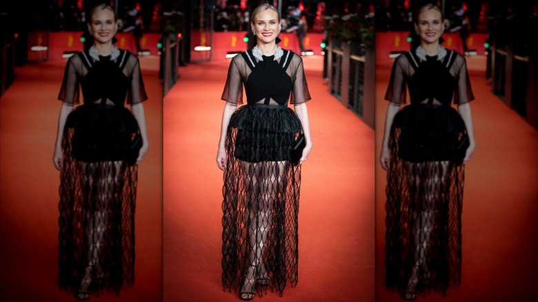 Diane Kruger på röda mattan klädd i en svart klänning med skira ärmar och svarta shorts täckta i en lång, svart spetskjol.
