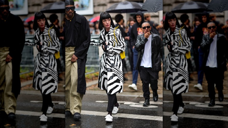 En kvinna under Paris Fashion Week 2024 bär en svart och vit randig regnjacka med vita slip-on loafers.