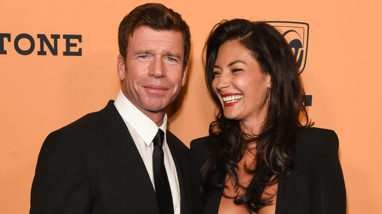 Taylor Sheridan deltar i ett Yellowstone-evenemang på röda mattan när fru Nicole Sheridan skrattar medan hon poserar bredvid honom.
