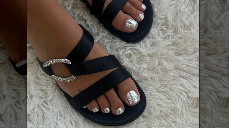 Närbild av en kvinnas fötter med en silverkrom pedikyr, klädd i svarta sandaler