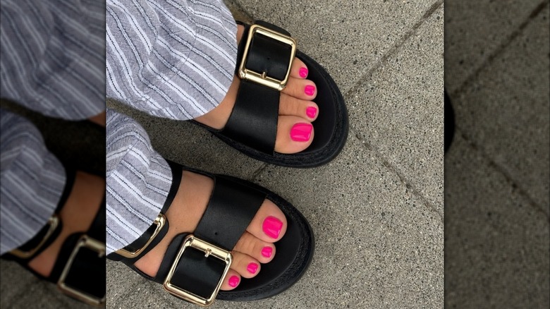 Närbild av en kvinnas fötter, klädd i rosa nagellack och tjocka svarta sandaler