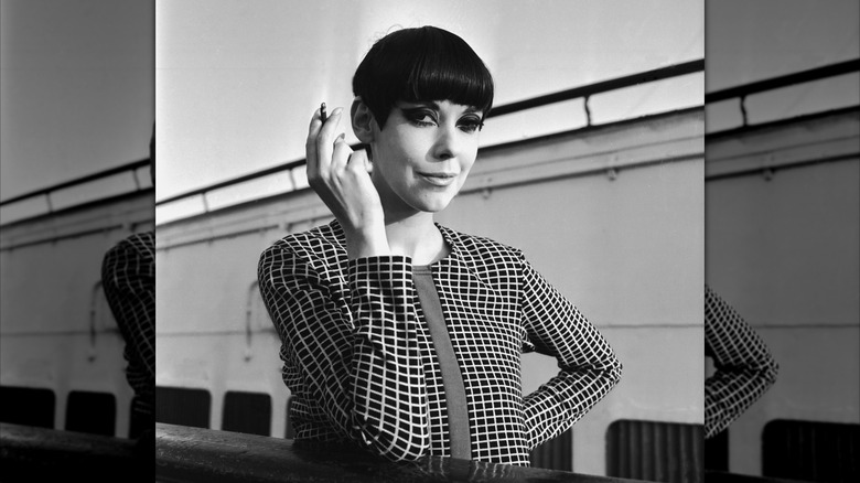 Ett porträtt av Peggy Moffitt som håller en cigarrett och ler i svart och vitt