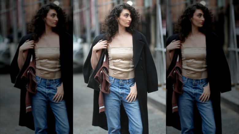 En kvinna bär en solbränd satin camisole, blå jeans och en svart ullrock.