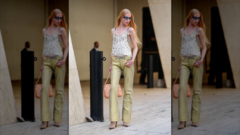 En modell på New York Fashion Week 2024 bär ljusgula jeans och en vit topp täckt av silverpaljetter.