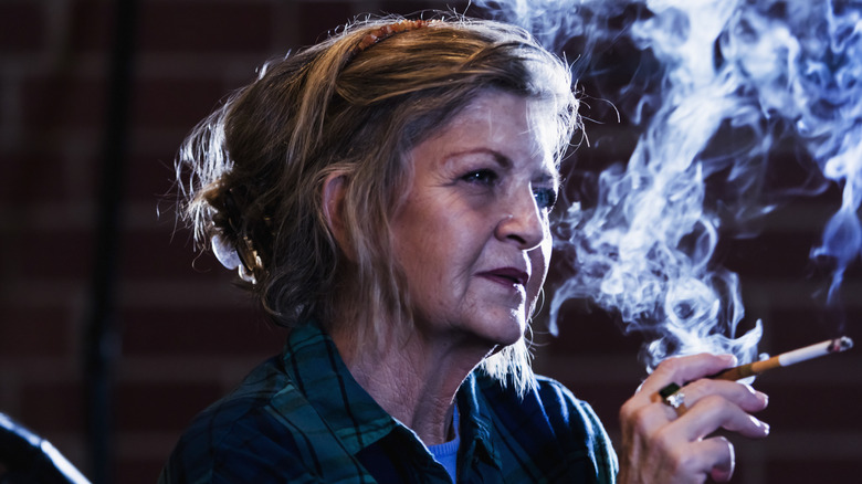 En kvinna i sextioårsåldern som röker en cigarett i ett mörkt rum